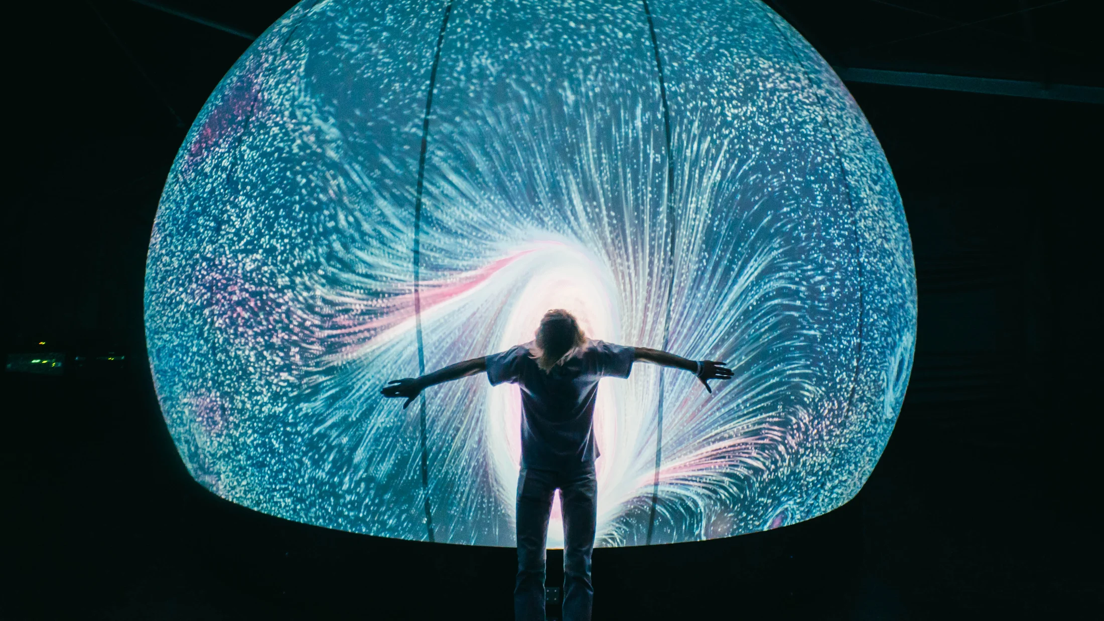 A visitor with arms outstretched before a luminous circular projection